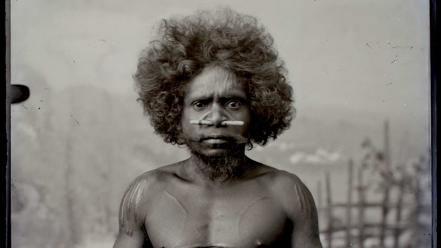 An Aboriginal man sits on a stool in a photography studio