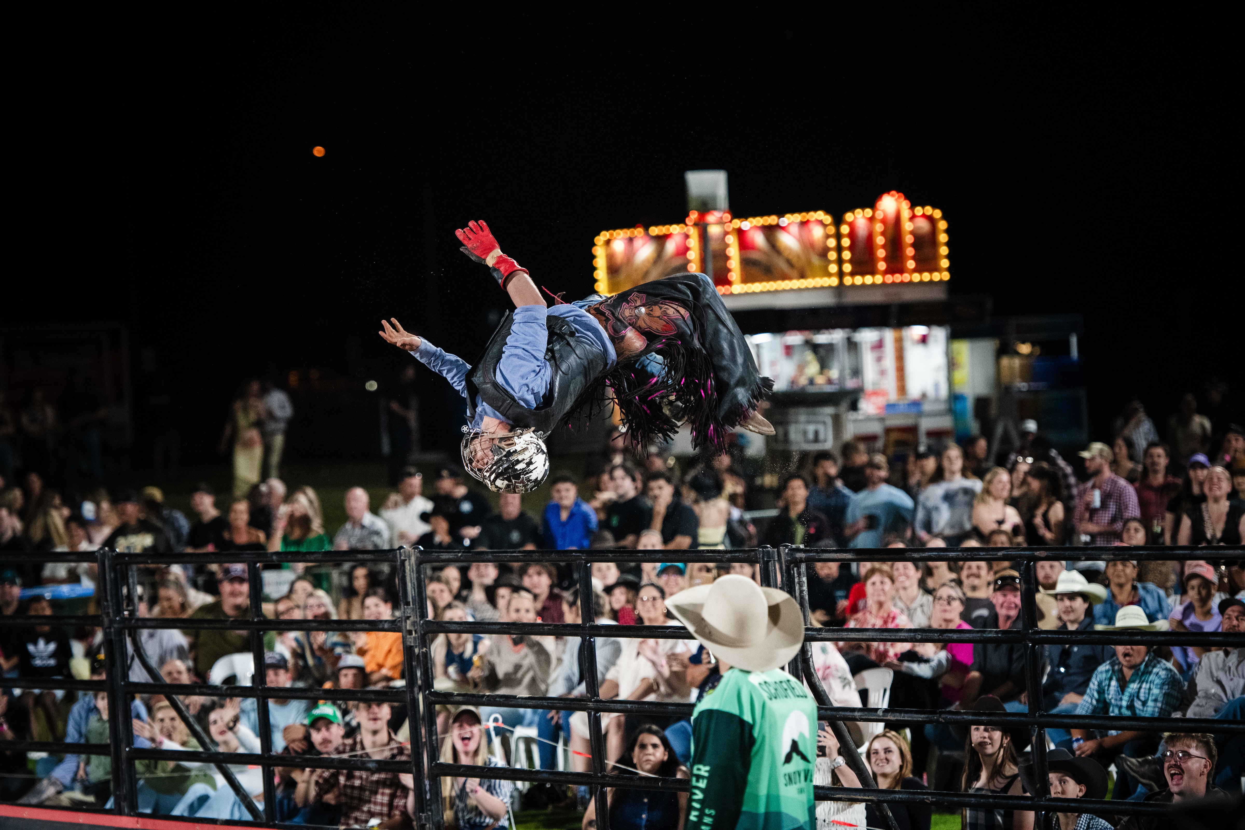 A cowboy backflips near a crowd.