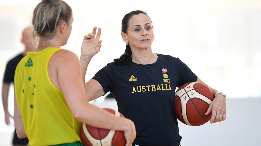Sandy Brondello speaks to an Opals player while holding a basketball.