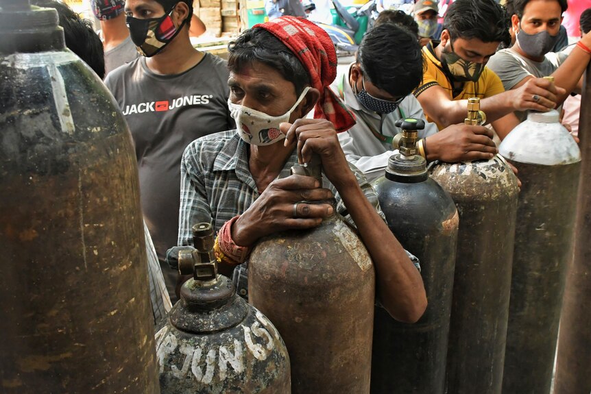 People wait in a queue with large oxygen cylinders 