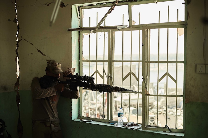 An Iraqi soldier aims a sniper rifle through a window.