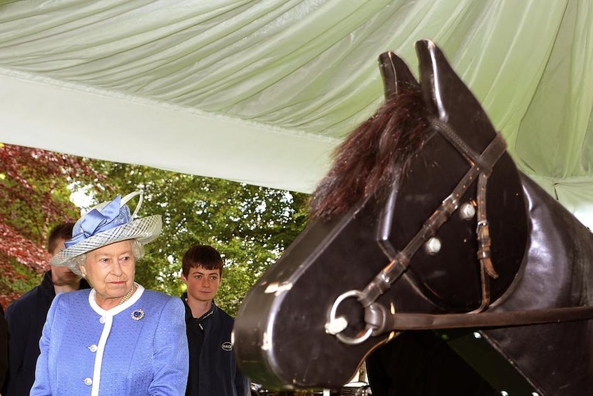 The Queen and Johnny Murtah watch a jockey demonstrate how mechanical horses are used