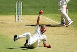 A New Zealand Test fast bowler grimaces as he lies on the pitch holding a pink ball aloft after taking a catch.