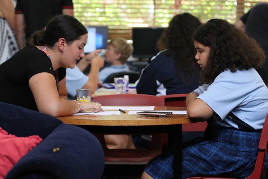 A teacher and a student talk over a table in a classroom.