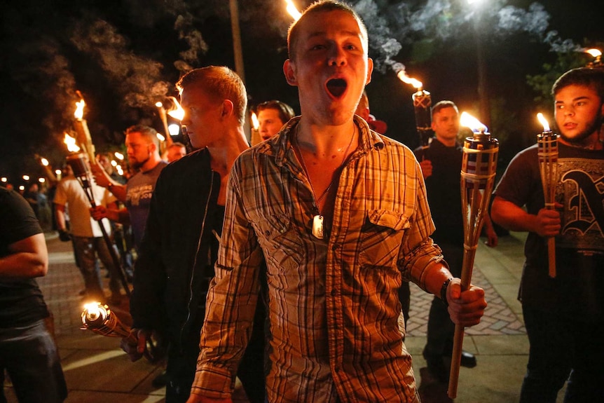 Young men holding torches march in the night.