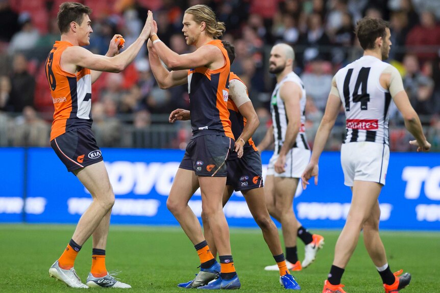 Two AFL players high-five in celebration after a goal, as their opponents walk past.