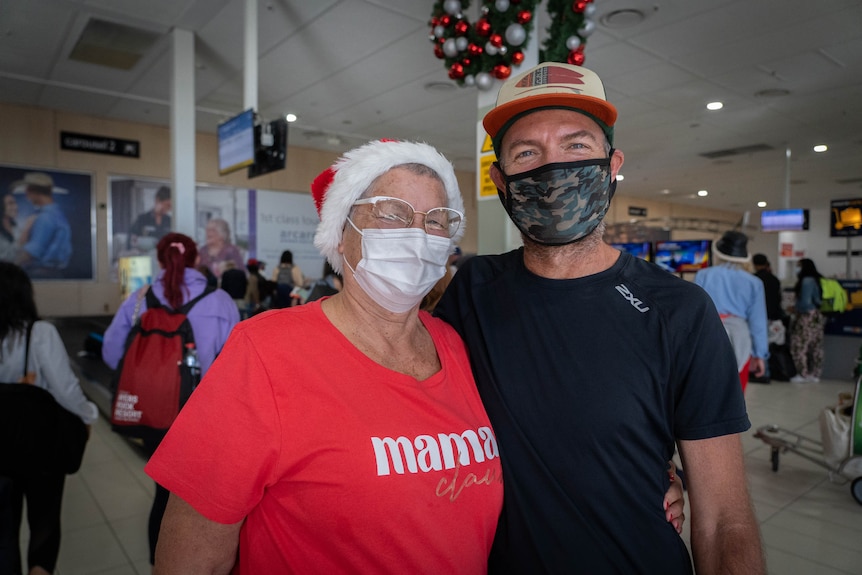 A woman in a santa hat and a man in a cap wearing masks.