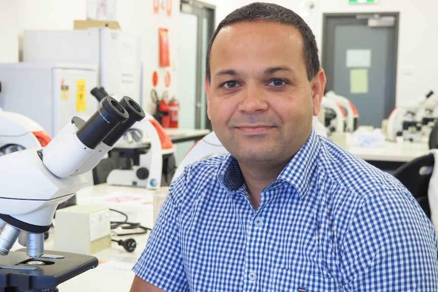 Dr Sukhwinder Sohal sits next to a microscope.