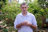 A man with short cropped hair stands in his backyard holding a small white bird.