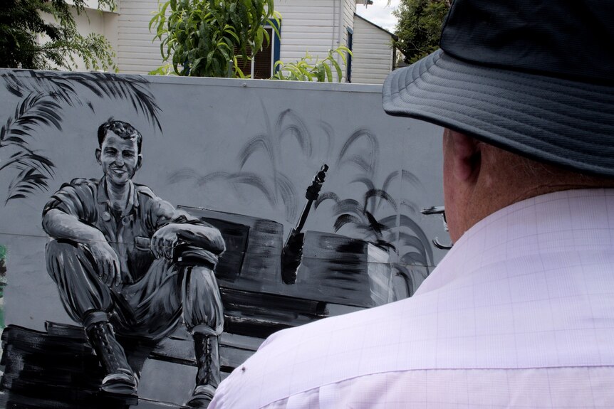 The back of a man's head as he looks towards a war mural. 