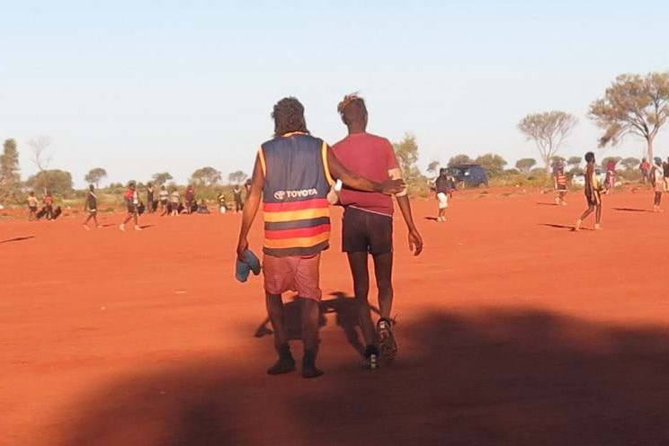Two indigenous football players, pictured from behind, walking together.