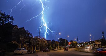 A bolt of lighting strikes from cloudy skies over a suburban street.