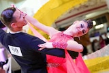 A male and female couple in ballroom attire dancing on the dance floor.