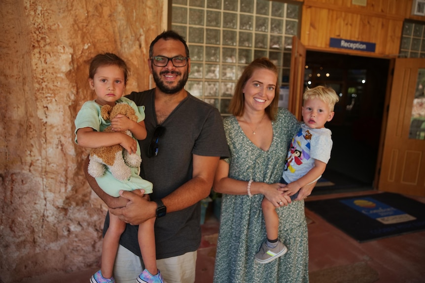 A smiling man holding a young girl in his arms stands next to a smiling woman with a young boy in her arms.