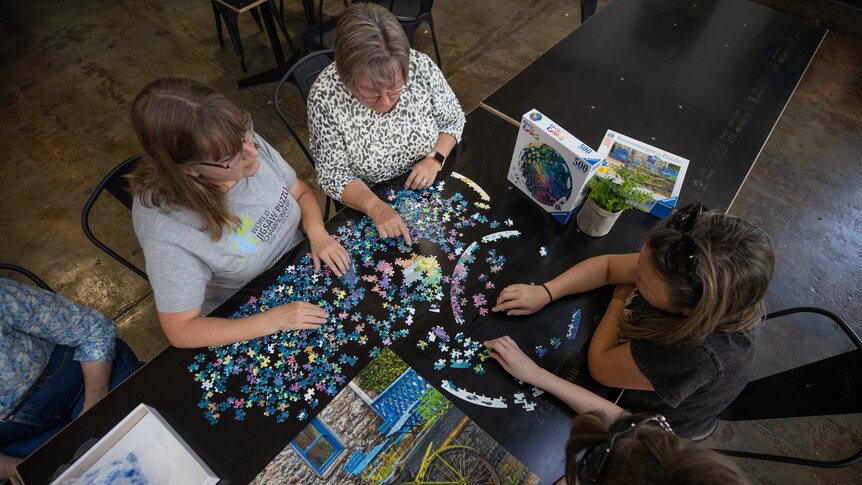 A photo taken from above of four people doing a jigsaw puzzle together on a black table