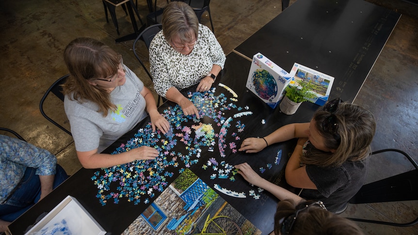 A photo taken from above of four people doing a jigsaw puzzle together on a black table