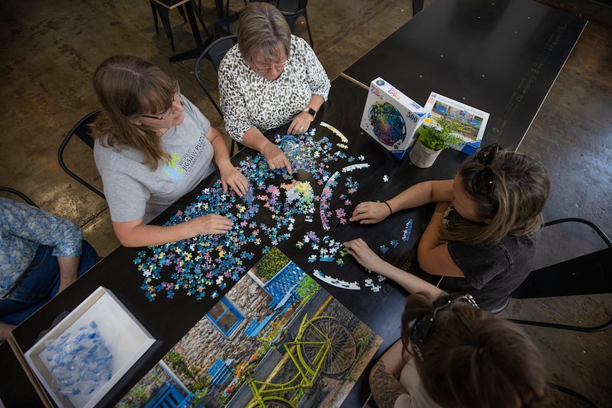 A photo taken from above of four people doing a jigsaw puzzle together on a black table