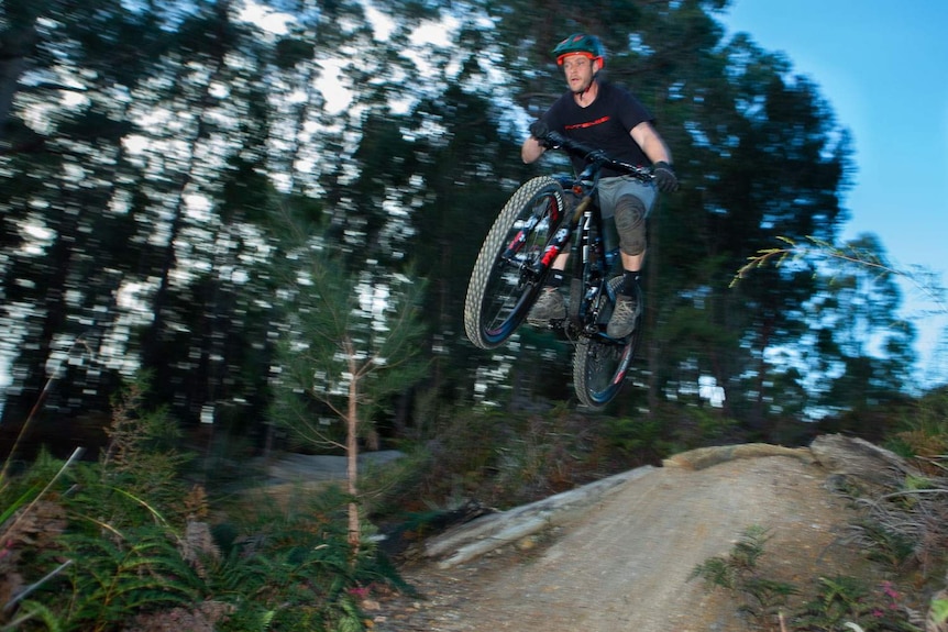 MTB rider mid flight over a jump on a bush trail
