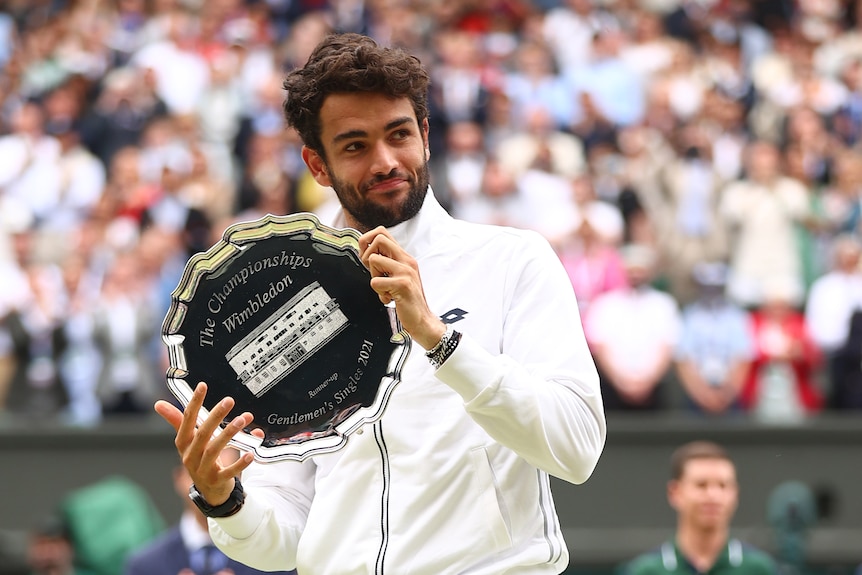 Mattero Berrettini holding a silver plate trophy and looking sideways