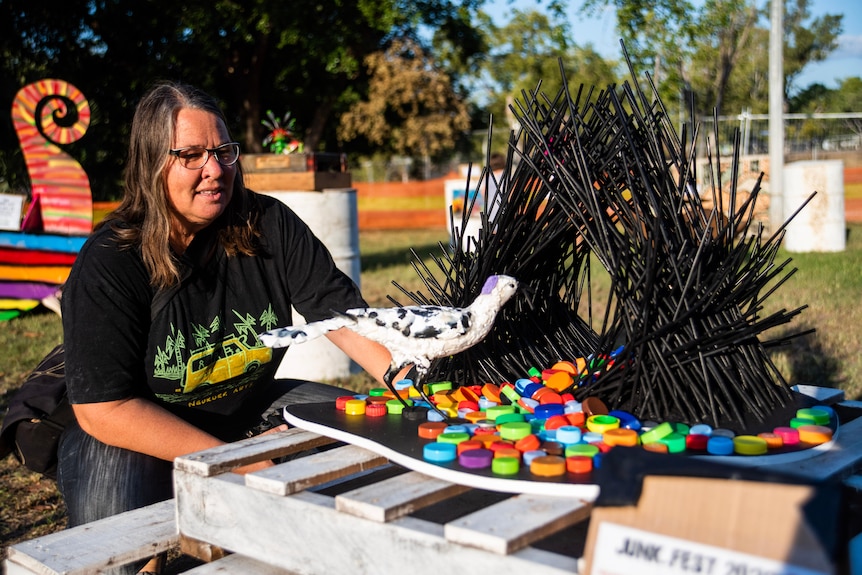 A woman looks at a bird sculpture made of plastic and straws. 