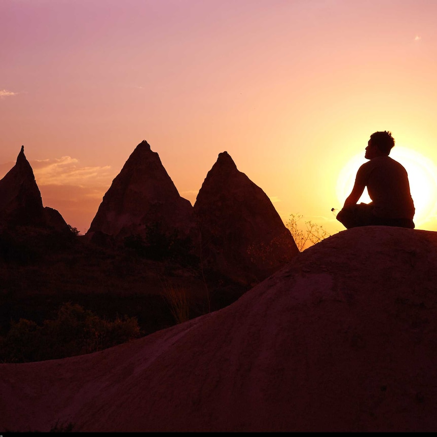 Man meditates in a mountain scenery at sunset.