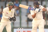 An Indian male Test batter hits a shot towards the leg side as the Australian wicketkeeper looks on.