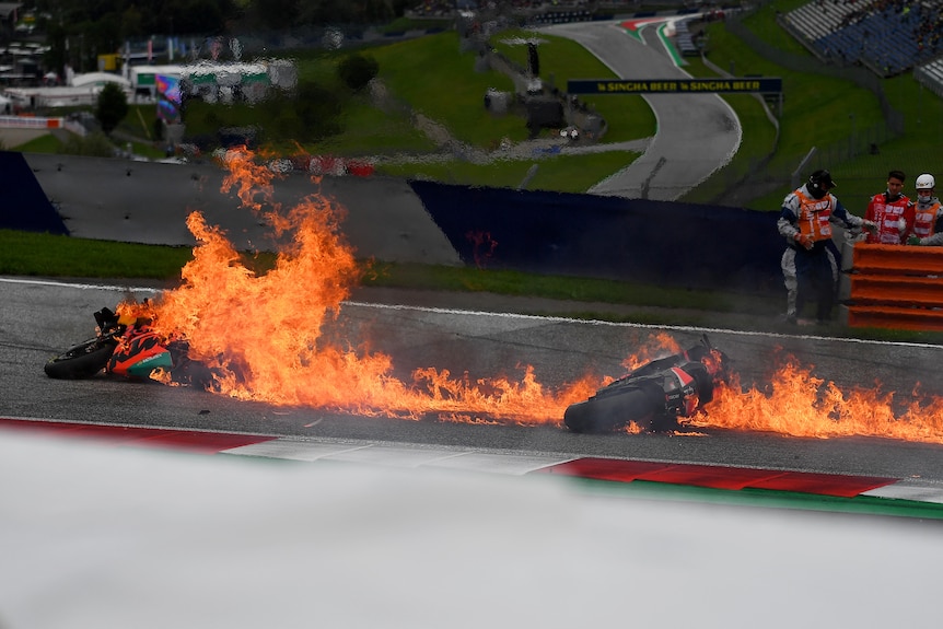 Two motorcycles are engulfed in flames on track.