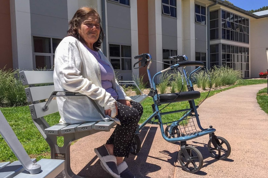 Elderly woman sitting on bench next to walking aid.