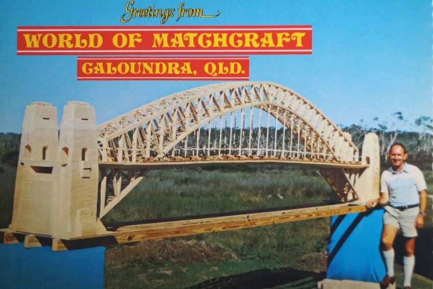 A postcard featuring a man standing next to large matchstick model of the arch-shaped Sydney Harbour Bridge.