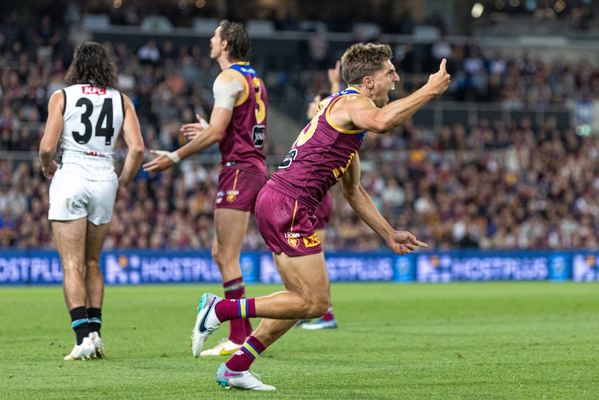 A Brisbane Lions player runs away from goal roaring in celebration while pointing his finger.