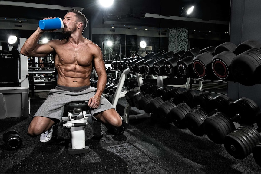 A scoop of protein powder with a tub in the backgroud.