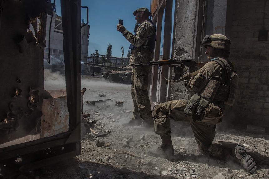 Two servicemen watch as a tank fires.