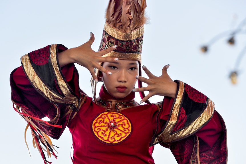 A woman in a red costume has her hands spread in front of her face as part of a performance. 