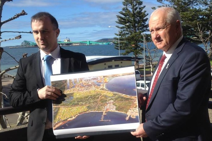 Two men in suits stand together holding a map.