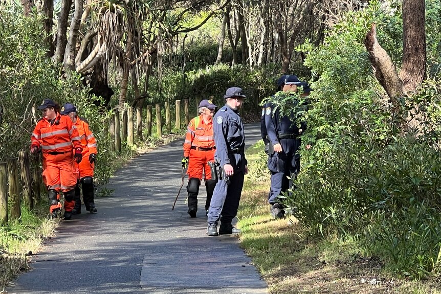 Police and SES personnel walking down a cement path with bushland on either side.