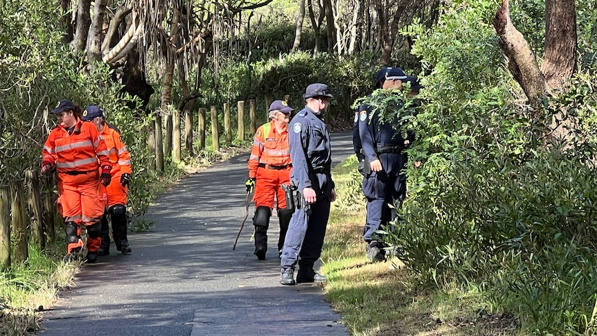 Police and SES personnel walking down a cement path with bushland on either side.