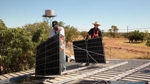 Two men carry solar panels on a tin roof