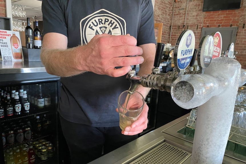 A man pours a Furphy beer from an icy tap behind the bar at a country pub.