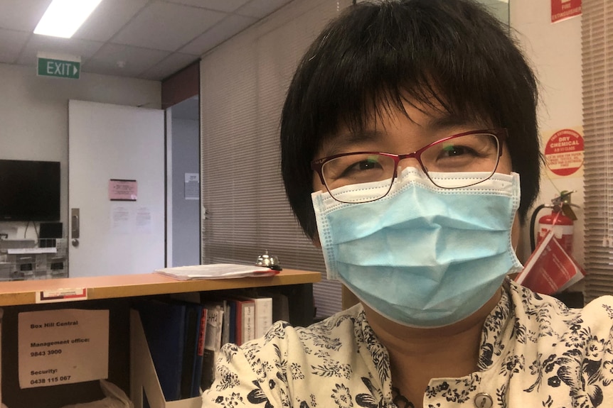 A woman wears a mask, standing in an office.