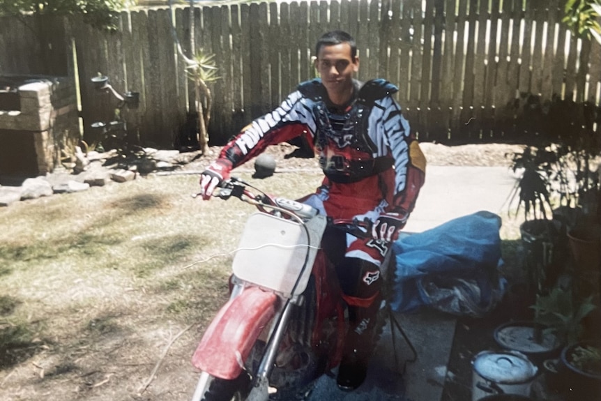 A young Indigenous boy sits on a motorbike in protective gear.