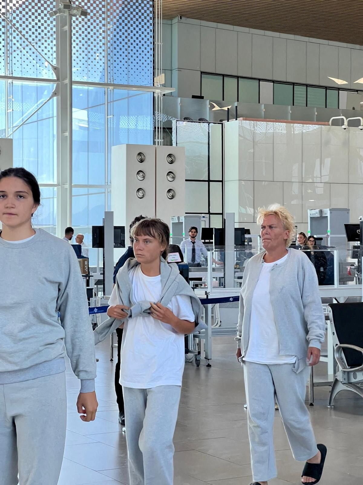 Greta Thunberg walks through an airport in a white shirt, pants and grey jumper