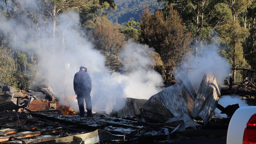 A man stands shrouded in smoke next to the remains of the inn.