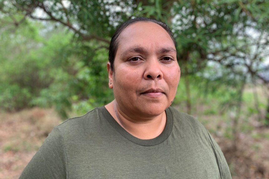an aboriginal woman with her hair pulled back, wearing a green shirt in the bush