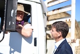 Angus Taylor stands outside a truck, speaking to a farmer in the cab. Hay bales sit on the tray.