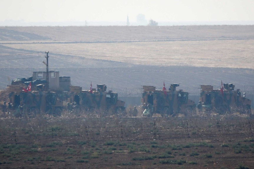 Three Turkish military vehicles, with the national flag on their roof, patrol a rural area