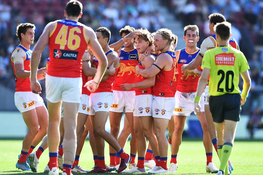 A Brisbane Lions player puts his arms around Will Ashcroft in congratulations after a goal, as his teammates surround him.