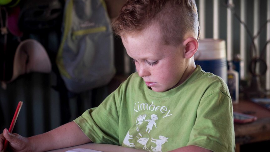 Young boy with red hair and green t-shirt does some writing work.