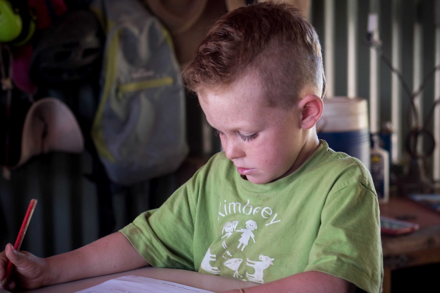 Young boy with red hair and green t-shirt does some writing work.