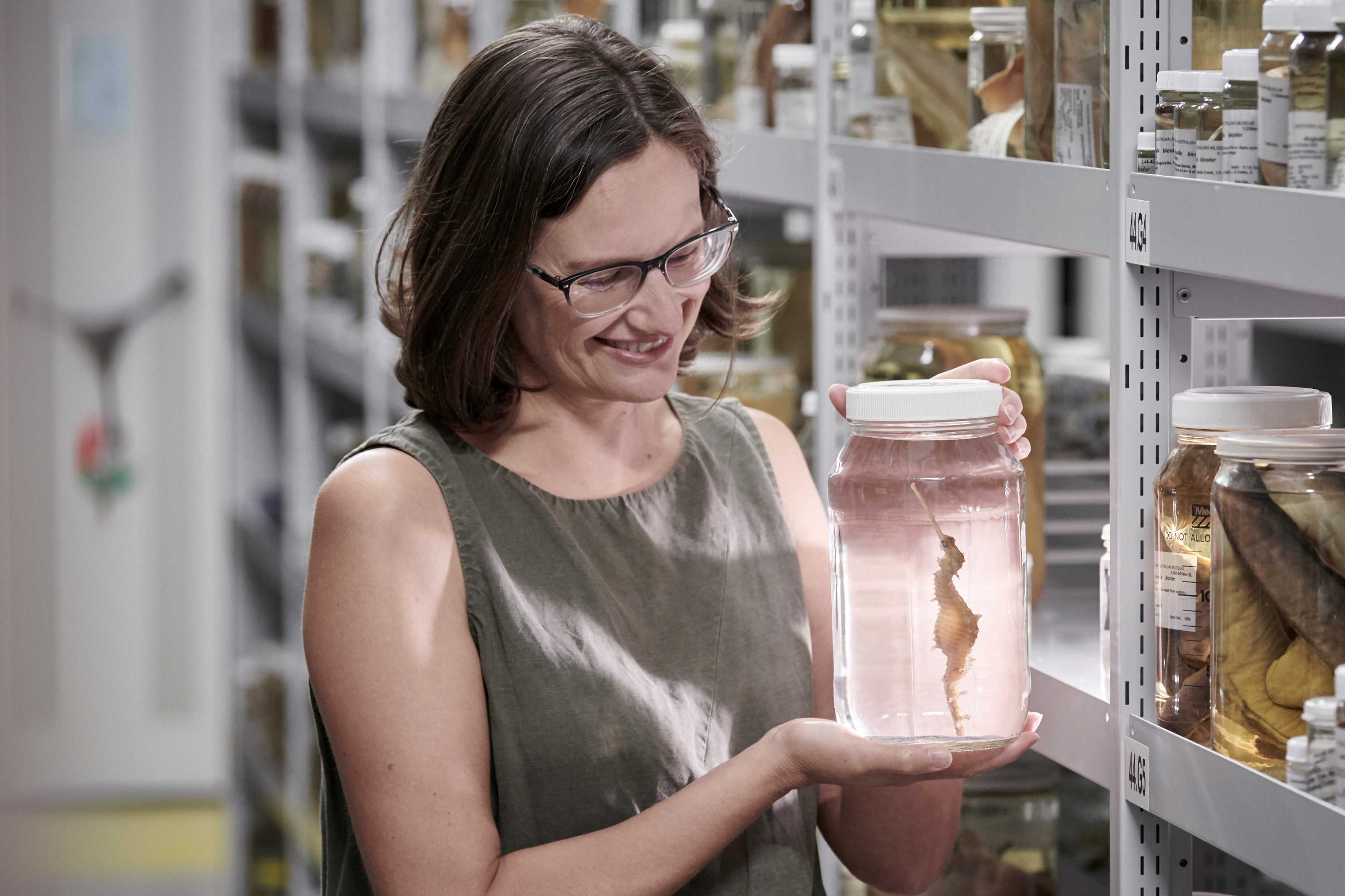 Nerida Wilson smiles and holds a jar with a seadragon specimen floating inside it.