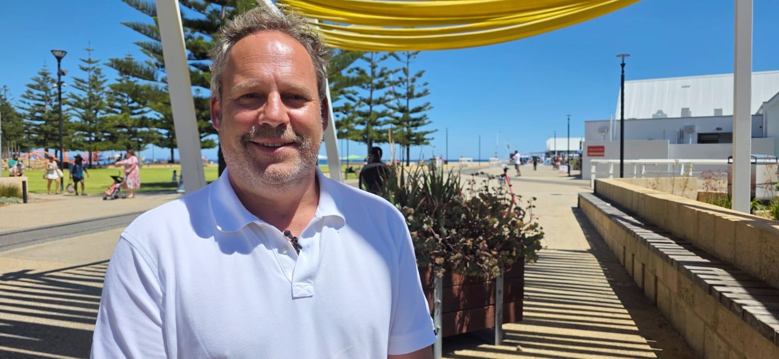 Um homem com uma camisa pólo branca está na praia de Busselton